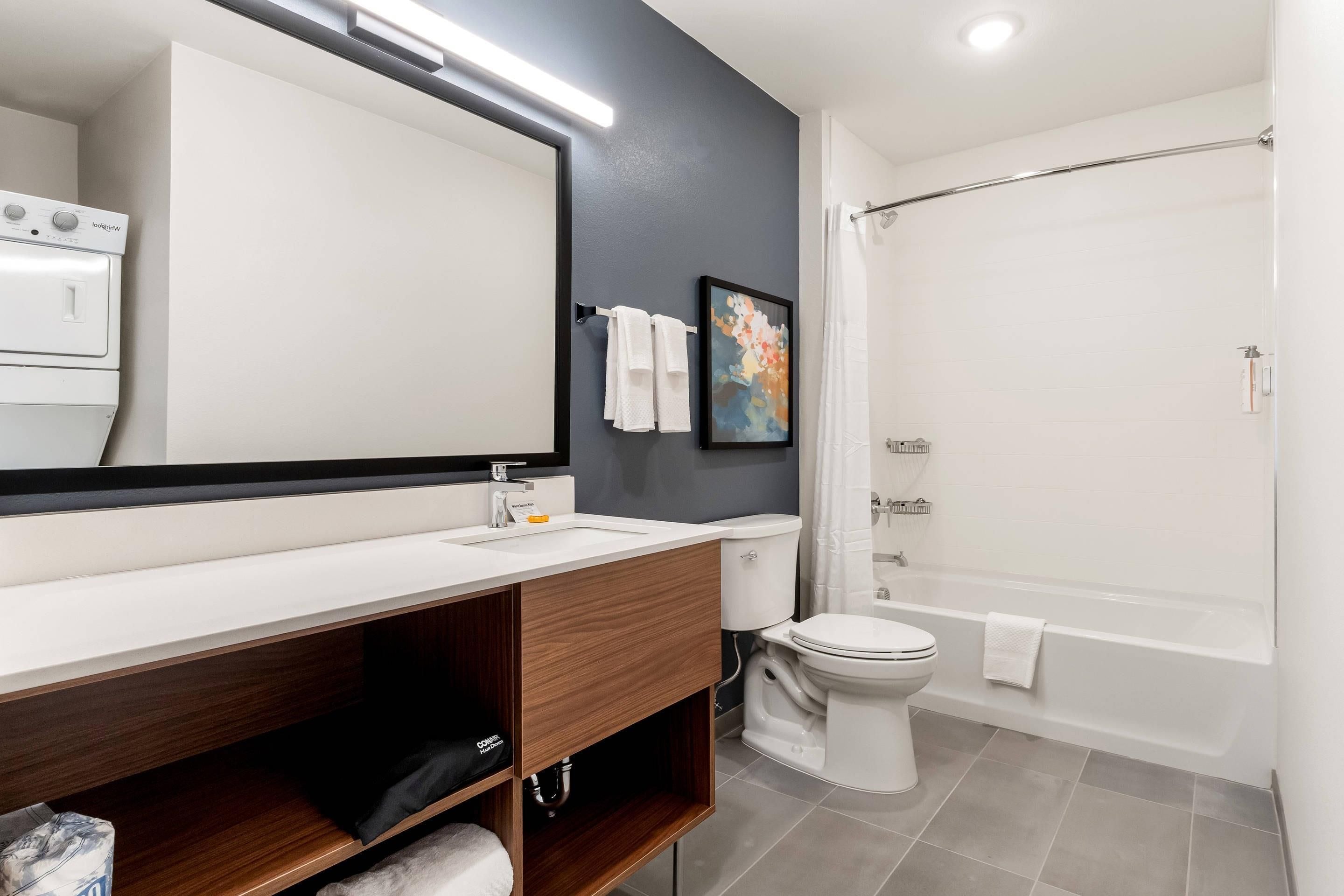 A modern bathroom with a white sink, a large mirror, a toilet, and a shower area.