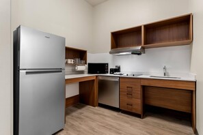 A compact kitchen with a refrigerator, microwave, coffee maker, and wooden cabinets. - Everhome Suites Denver Airport (Denver)