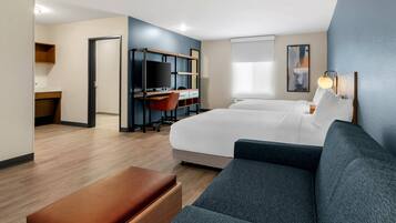 A hotel room with a bed, a desk with a TV, a sofa, and a window.