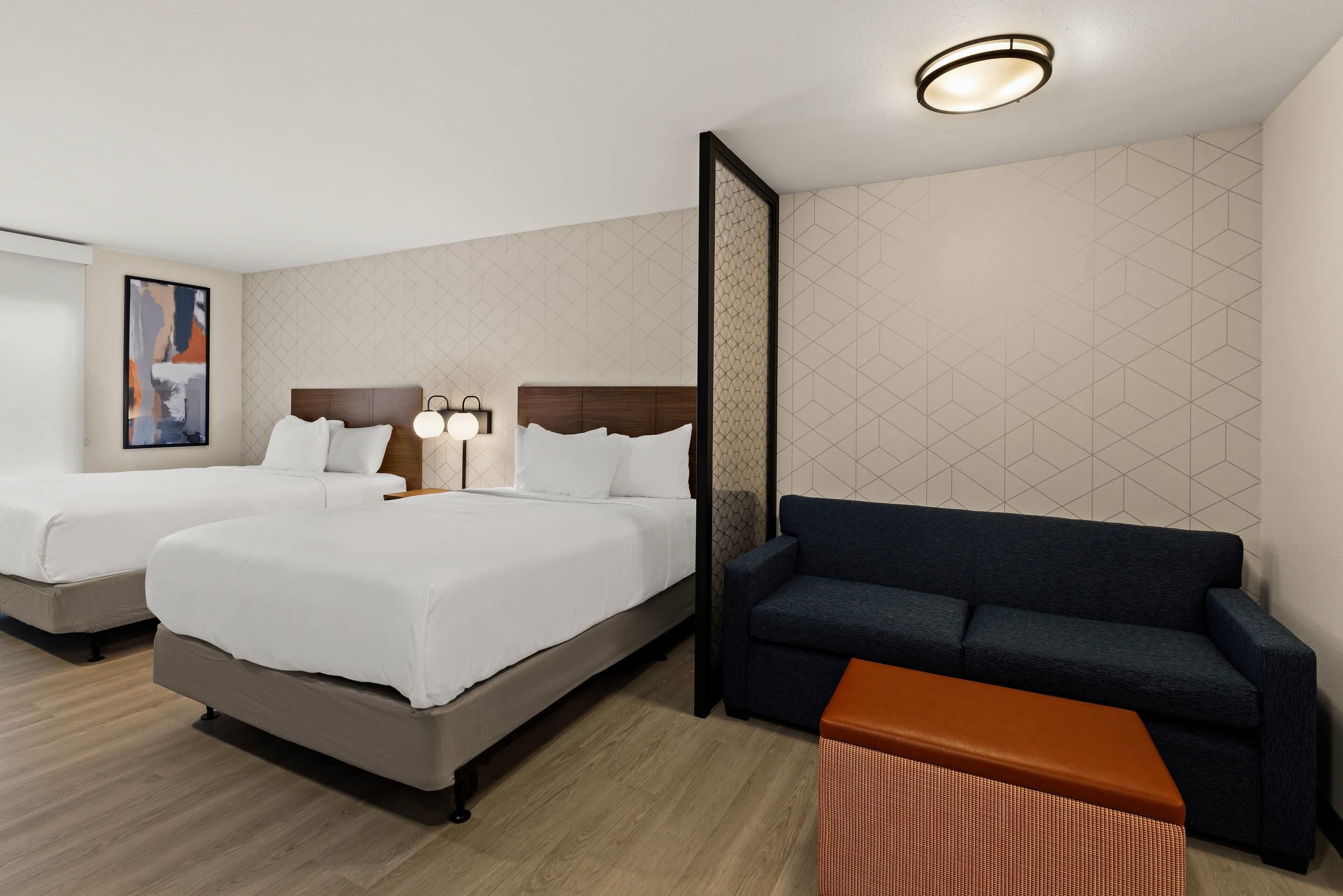 A hotel room with two beds, a sofa, a small table, and a wall with geometric patterns.