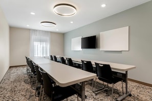 A conference room with a long table, chairs, a large window with curtains, and two mounted screens on the wall. - Everhome Suites Denver Airport (Denver)