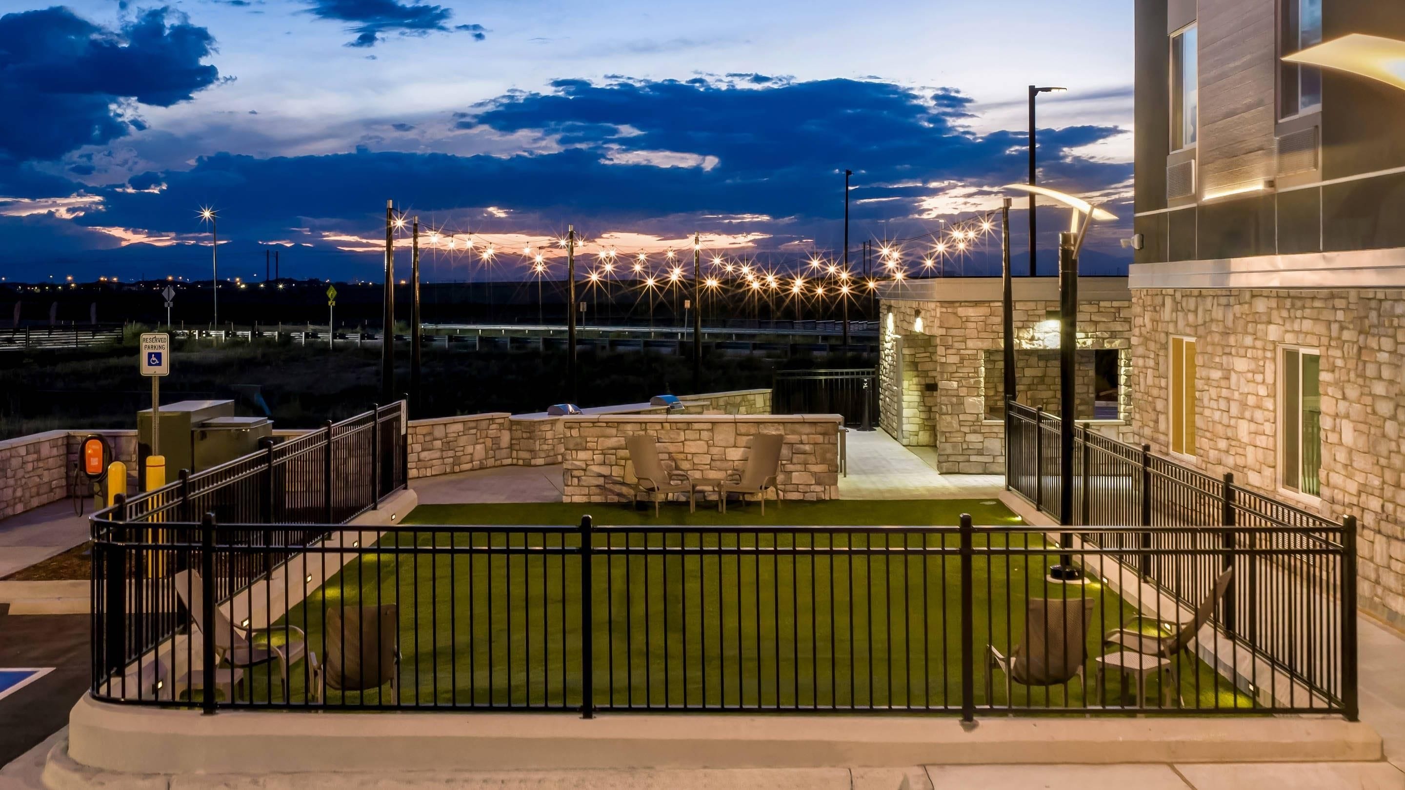 A rooftop patio with a stone wall, outdoor seating, and a view of the cityscape at dusk.