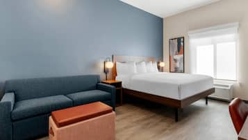 A hotel room with a bed, a sofa, a small ottoman, a nightstand, and a window.