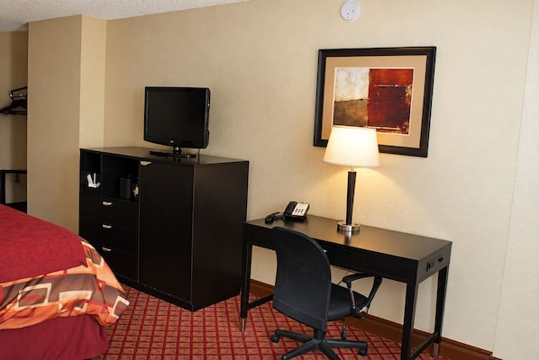Een hotelkamer met een bed, een bureau met lamp, een telefoon, een televisie op een kast, en een lijstje aan de muur.