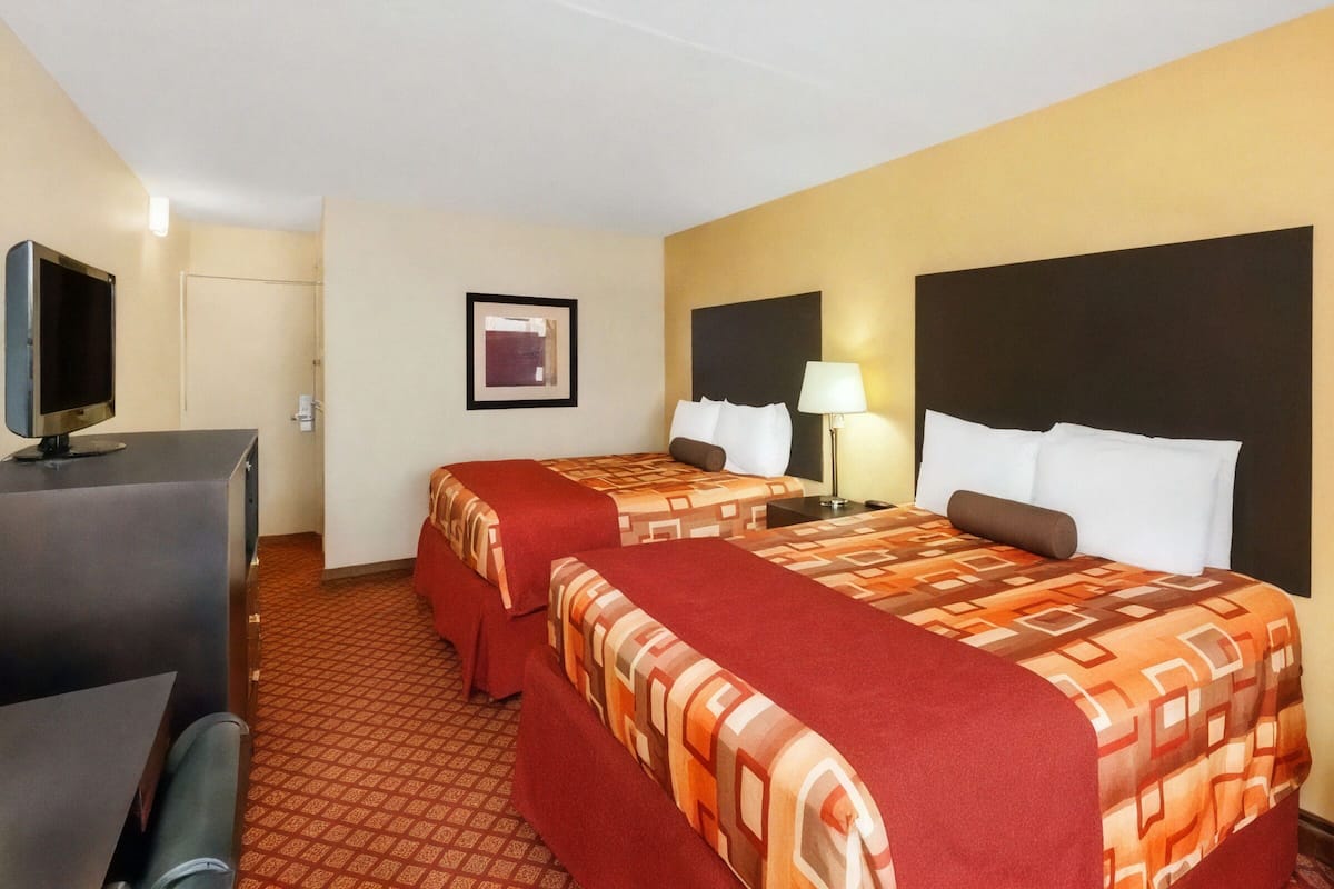 A hotel room with two beds, a desk, a television, and a framed picture on the wall.