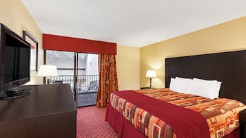 A hotel room with a bed, a desk with a TV, a balcony, and a window.