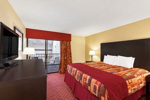 Una habitación de hotel con cama, escritorio con televisor, balcón y ventana.