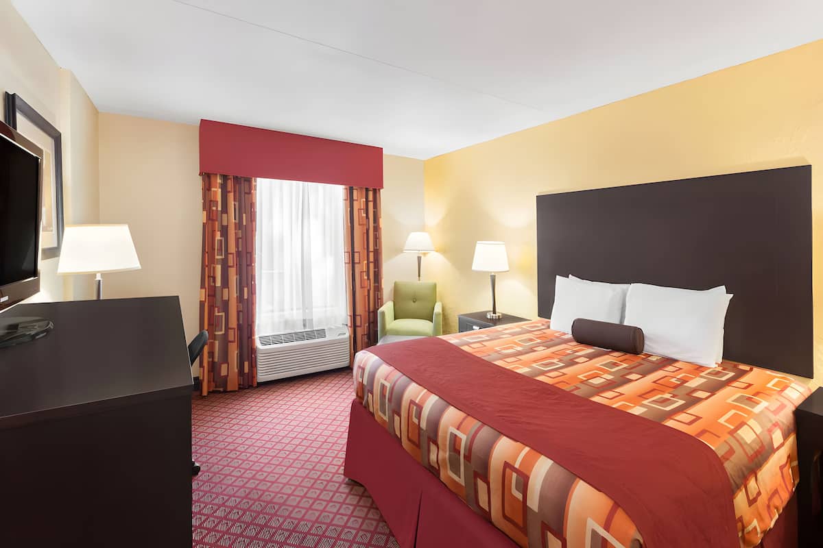 A hotel room with a bed, a desk, a chair, a TV, and a window with curtains.