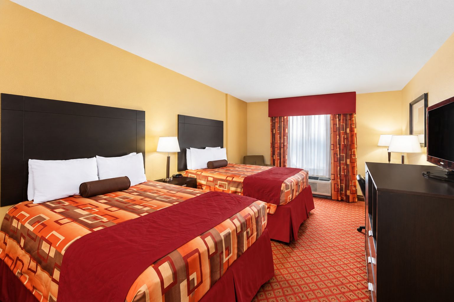 A hotel room with two beds, a desk, a television, and a window with curtains.