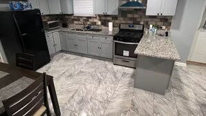 Une cuisine moderne avec des meubles gris, un réfrigérateur noir, un four à micro-ondes, une cuisinière et un coin repas comprenant une table et des chaises.