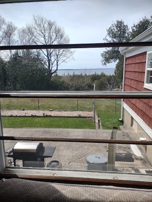 Une vue à travers une fenêtre donnant sur une cour arrière avec une pelouse, un barbecue et une maison aux murs recouverts de bardage rouge.