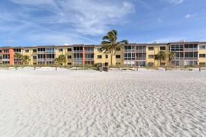 A beachfront hotel with multiple-story buildings, a sandy beach in the foreground, and palm trees. - NEW! Beachfront Ground Floor: Million $ Views (Sarasota)