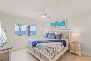 Ein Schlafzimmer mit einem Bett, einem Nachttisch, einem Fenster mit Meerblick und einem Deckenventilator.