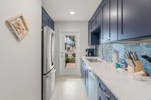 A modern kitchen with dark blue cabinets, a white refrigerator, a tiled backsplash, and a countertop with kitchen utensils. - Gulf-to-Bay Luxury: Million Dollar Views at this Newly Remodeled Beachfront Ground Floor Condo (Sarasota)