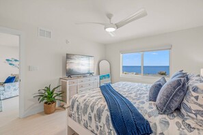 A bedroom with a bed, a television, a window with a view of the sea, a ceiling fan, and a plant. - NEW! Beachfront Ground Floor: Million $ Views (Sarasota)