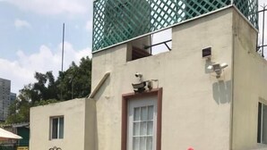A building with a flat roof, a door, and a small window. There are potted plants and a bench outside. - The 222 (Mexico City)