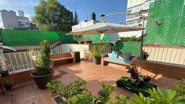 A rooftop patio with wooden flooring, outdoor furniture, potted plants, and a green mesh wall. - The 222 (Mexico City)