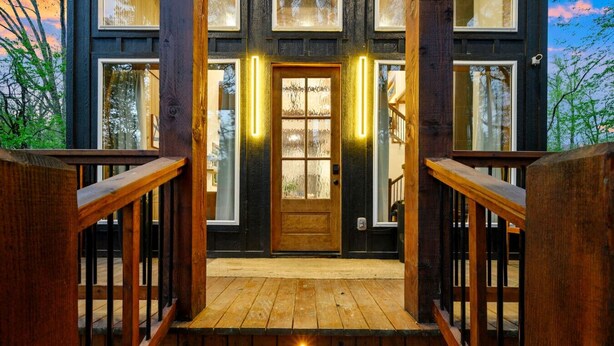 Una scala in legno conduce a una porta d'ingresso con pannelli di vetro e un lampadario sopra.