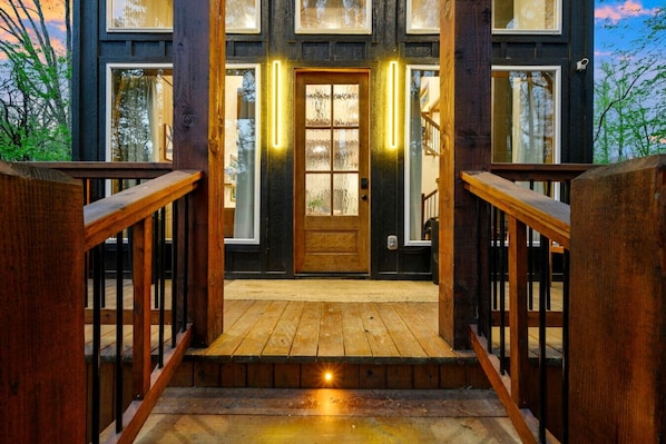 A wooden staircase leading to a front door with glass panels and a light fixture above it. - Moonlit Waves · New! Pond + Deck | Hot Tub, Fire Pit & Cozy Cabin (Broken Bow)