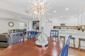 A modern kitchen with white cabinets, a central island, and a dining area with blue chairs. - A Hidden Paradise Right Across from Indian Rocks Beach! (Indian Rocks Beach)