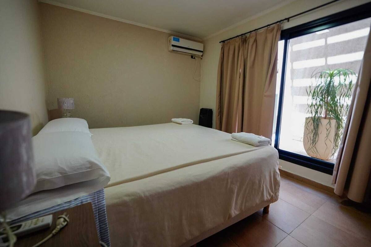 Habitación de hotel con cama, lámpara, equipo de aire acondicionado, altavoz y ventana con cortinas.