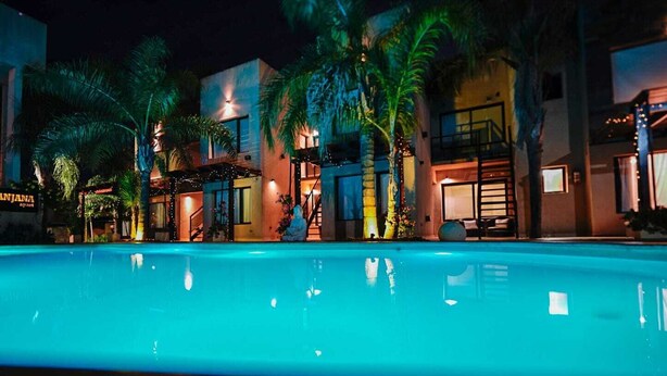 A swimming pool with a night-time view of buildings, palm trees, and a staircase. - Complejo Anjana (Federación)
