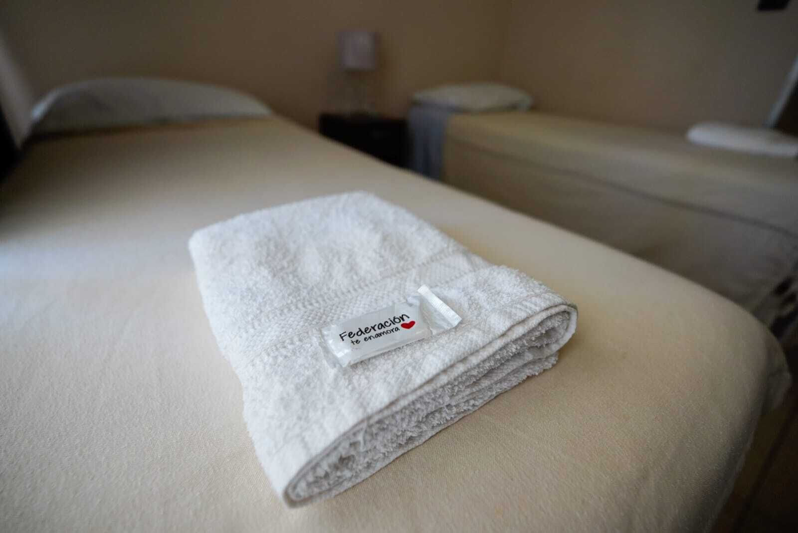Una toalla blanca doblada con cuidado, con una etiqueta sobre la cama en una habitación de hotel.