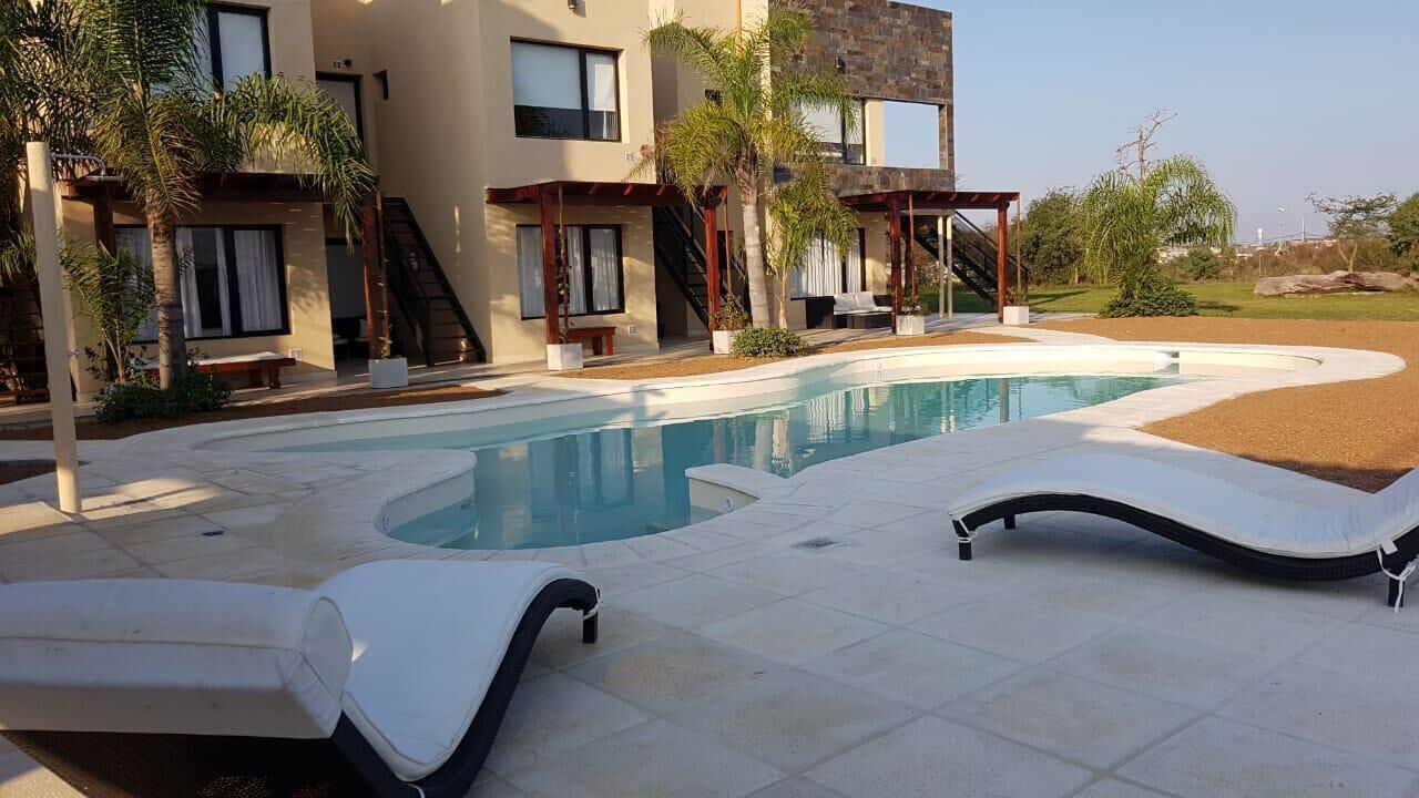 Un área de piscina moderna con sillones de descanso, piscina e inmueble de varios pisos con balcones.