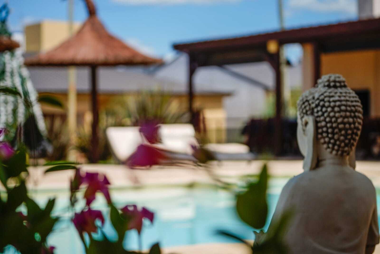 A Buddha statue by a pool with a thatched roof structure in the background.