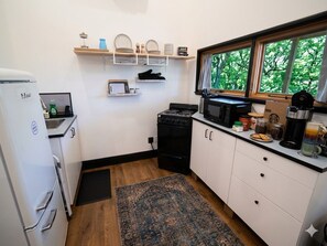 Eine kleine Küche mit Kühlschrank, Herd, Mikrowelle und einem Fenster mit Blick auf Bäume.
