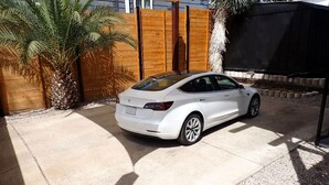 A white car parked in a driveway with a palm tree and wooden fence in the background. - Rooftop Movie House w/ Stunning views ❤️ East Austin Studio | Free Parking (Austin)