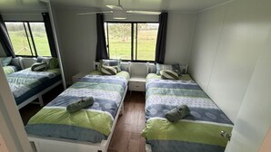 Ein Zimmer mit zwei Einzelbetten, einem Deckenventilator und einem Fenster mit Blick auf eine Rasenfläche.