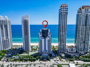 A high-rise hotel with a prominent location marker, surrounded by other tall buildings and a beach. - Exclusive Trump Beachfront Condo (Sunny Isles Beach)
