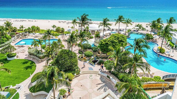 Un resort con varias piscinas, palmeras y vista a la playa.