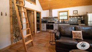 Un área de estar tipo loft con una escalera de madera, un sofá de cuero y una cocina al fondo.