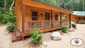 Una cabaña de madera con porche, rodeada de árboles y grava.