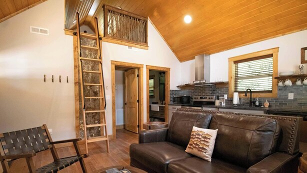 Un interior acogedor con techo de madera, un sofá de cuero marrón, una escalera de madera y una zona de cocina con salpicadero de ladrillo.