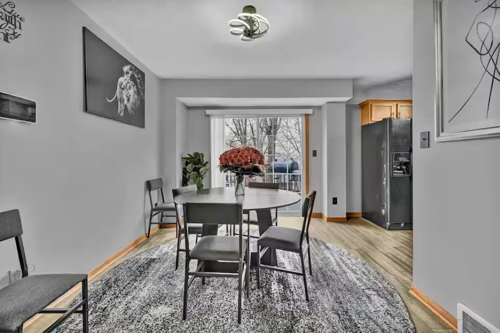 Een moderne keuken met een koelkast, een eethoek met een ronde tafel en stoelen, en een groot raam met uitzicht op bomen.