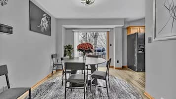 Een moderne keuken met een koelkast, een eethoek met een ronde tafel en stoelen, en een groot raam met uitzicht op bomen.