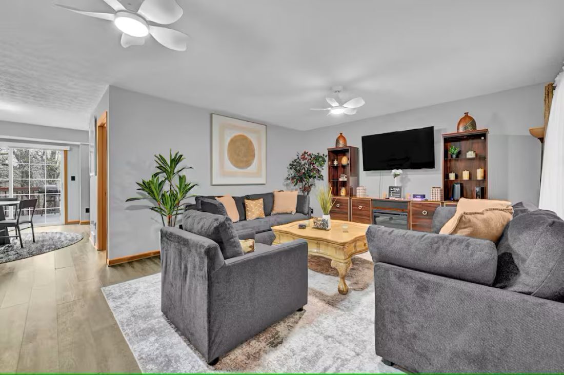 Een moderne woonkamer met een grijze zithoek, een salontafel, een televisie en een boekenkast.