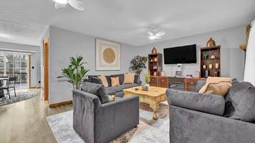 Een moderne woonkamer met een grijze zithoek, een salontafel, een televisie en een boekenkast.