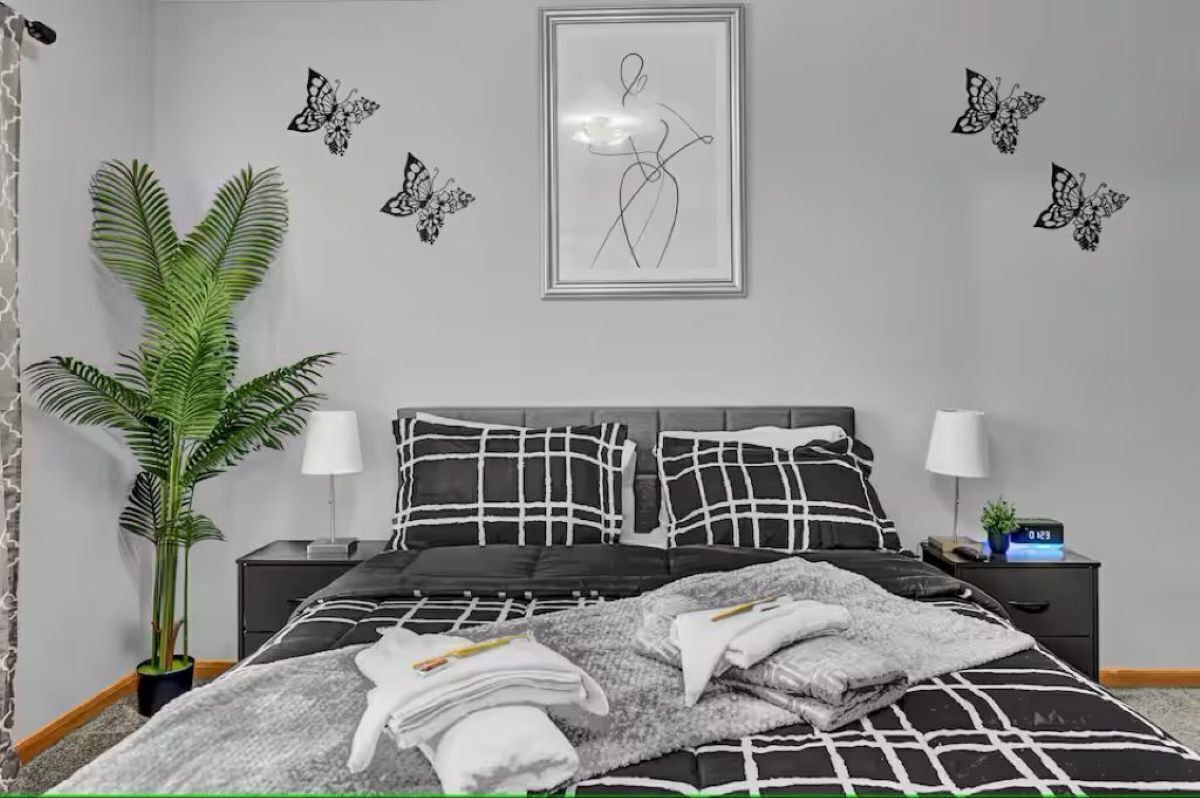 Een slaapkamer met een bed, twee nachtkastjes, een potplant en wanddecoratie.