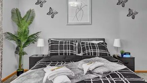 Un dormitorio con una cama, dos mesitas de noche, una planta en maceta y decoración en la pared.
