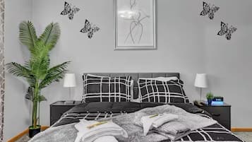 Een slaapkamer met een bed, twee nachtkastjes, een potplant en wanddecoratie.