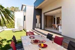 An outdoor dining area with a table set for two, surrounded by chairs, and a view of the adjacent building. - Villa Amphitrite • Share, beach & happiness (Agde)