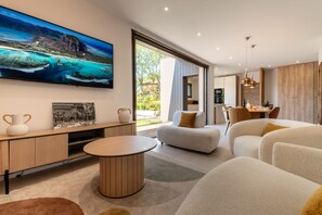 A modern living room with a large TV, comfortable seating, and a view of the outdoors. - Villa Amphitrite • Share, beach & happiness (Agde)
