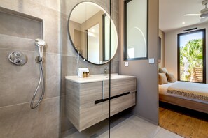 A modern bathroom with a glass-enclosed shower, a round mirror, and a wooden vanity. - Villa Amphitrite • Share, beach & happiness (Agde)
