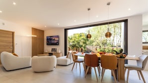 Een moderne woonkamer met een eethoek, grote ramen en uitzicht op groen.