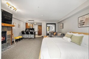 Una habitació d'hotel moderna amb una llar de foc, zona de menjador, sofà i llit.