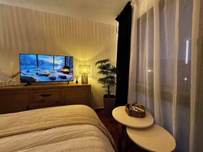 A hotel room with a bed, a TV displaying a winter scene, a bedside table with a lamp, and a plant. - Snow&sun home (Sierra Nevada)